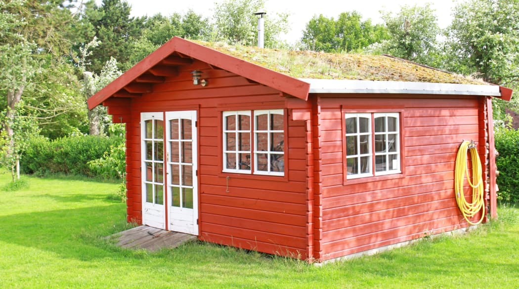 Rotes Holz-Gartenhaus mit extensivem Gründach.
