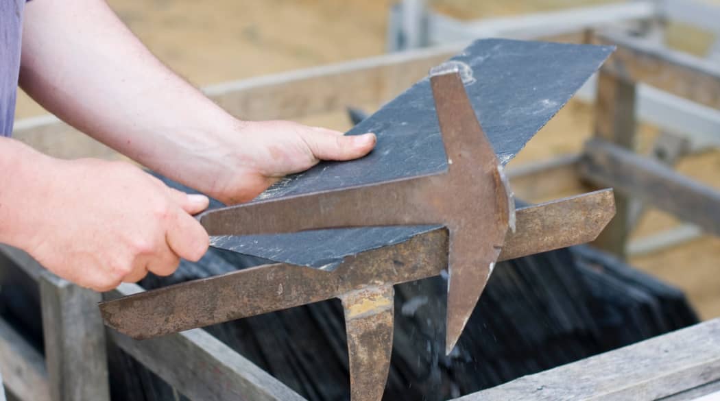 Ein Dachdecker bringt einen Schieferstein mit einem Schieferhammer in die richtige Form.