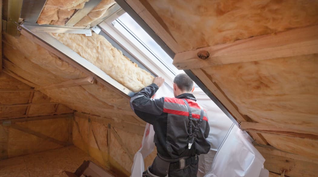 Das Dach sanieren: Ein Mann dämmt ein Dachfenster