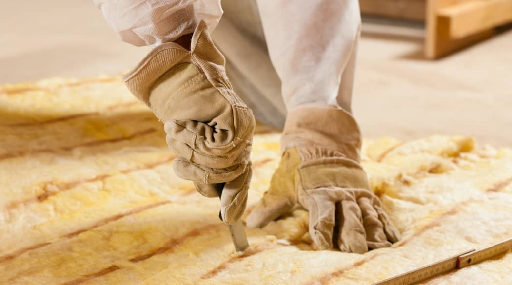 Ein Handwerker schneidet mit einem Messer Glaswolle für eine Dachdämmung.