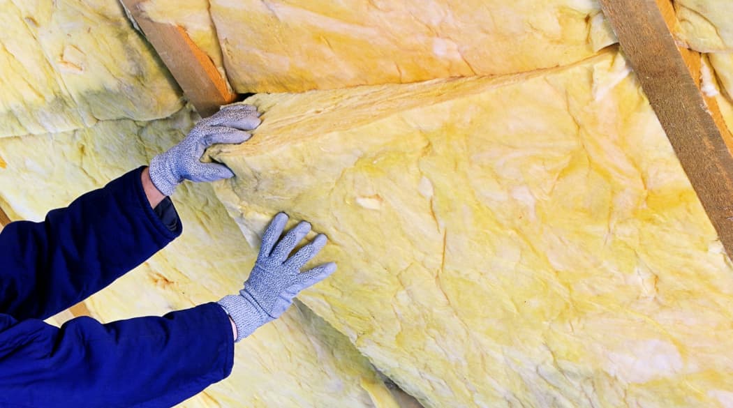 Handwerker dämmt ein Satteldach mit Mineralwolle.