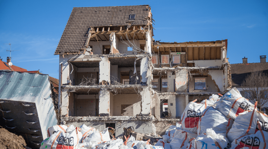 Ein abgerissenes Haus mit mehreren weißen Asbest-Säcken im Vordergrund