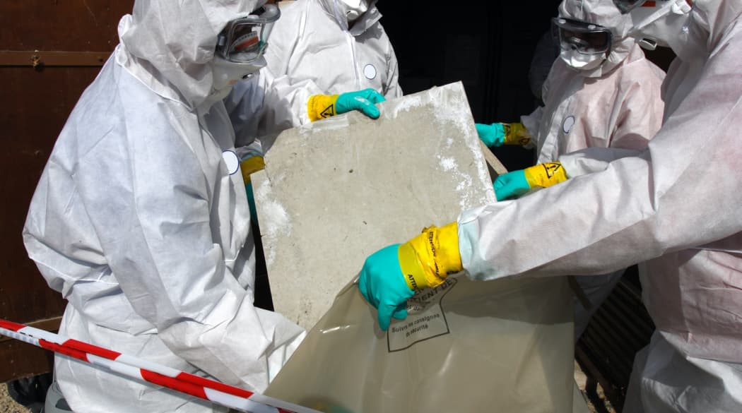 Handwerker entfernen alte Asbestplatten in einem Sack.